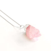 Close up view of rose quartz love crystal pendant with stainless steel snake chain.